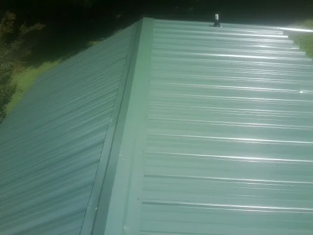 New green metal panels meeting at the ridge of a roof — Flat Roof Repair work by our crew in Nineveh