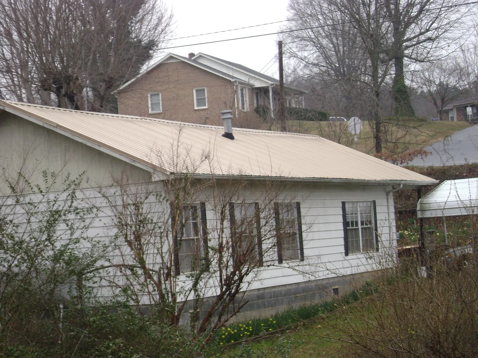 Tan metal roof on a white sided house set into a hillside — Commercial Roofing by Roofing Brothers in Nineveh